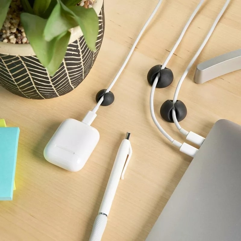 A desktop with a plant, cable organizer, AirPods, and a pen on it; essentials for a tidy workspace