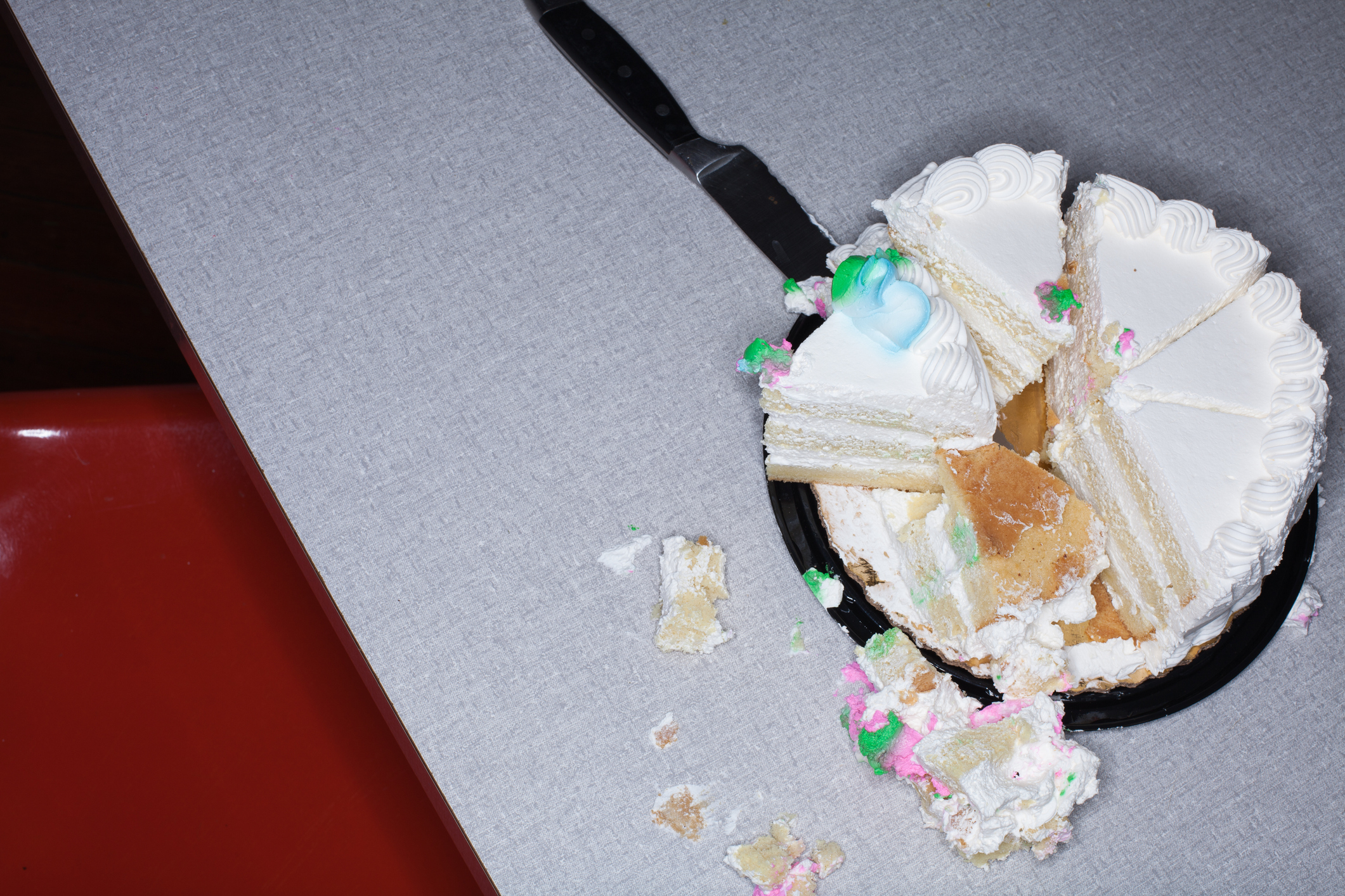 A partly eaten cake with one slice on a spatula, messy icing and crumbs on table