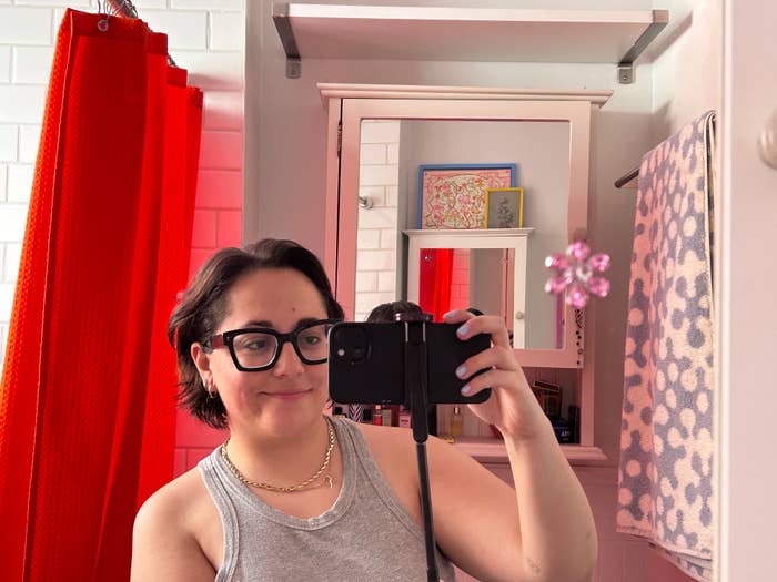 Person taking a mirror selfie with a camera, standing in a bathroom with visible decor and accessories