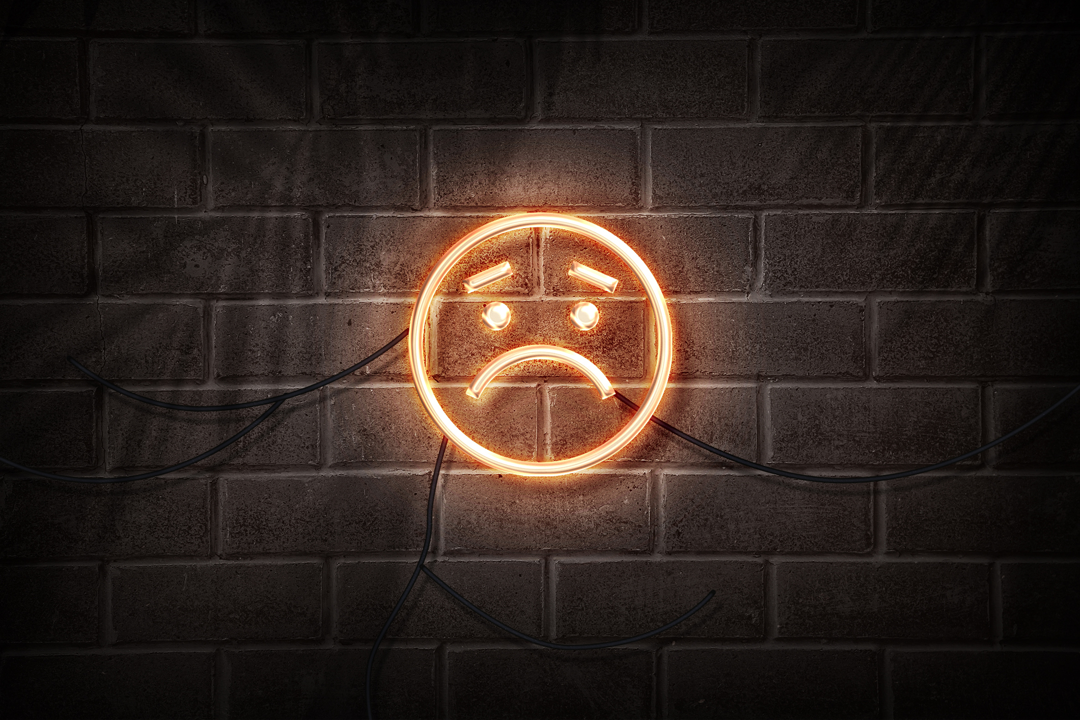 Neon sign of a frowning face on a brick wall