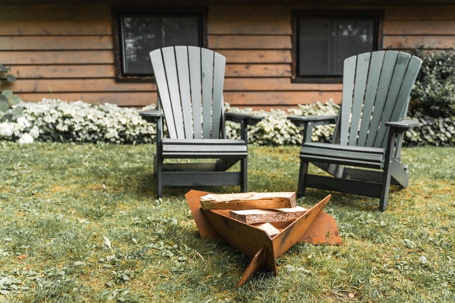 Two wooden Adirondack chairs facing a small fire pit in a backyard setting