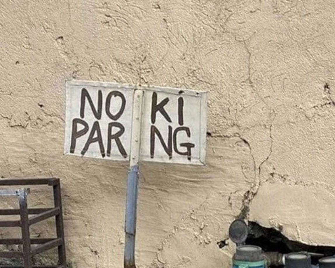 Handmade sign on a wall with the words &quot;NO PARKING&quot; split unevenly between two pieces of metal