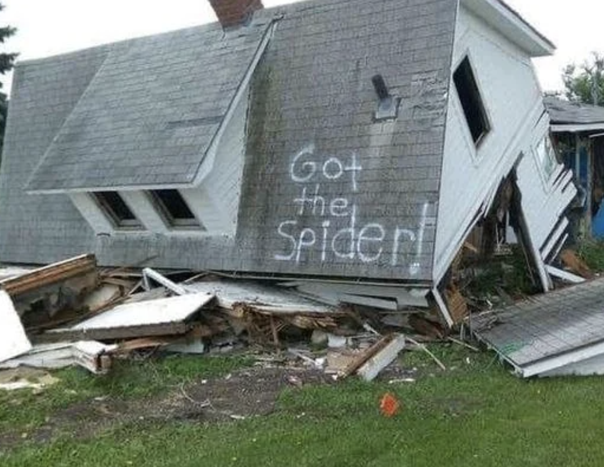 A collapsed house with &quot;Got the spider!&quot; spray-painted on the side