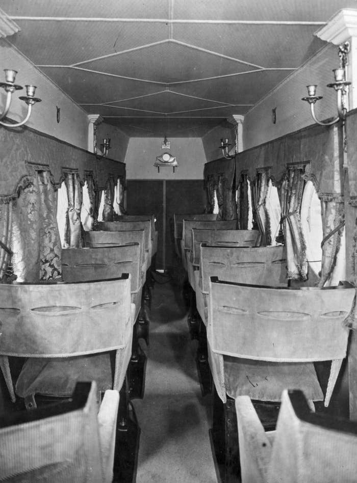 Interior of an old train carriage with rows of wooden seats and overhead luggage racks