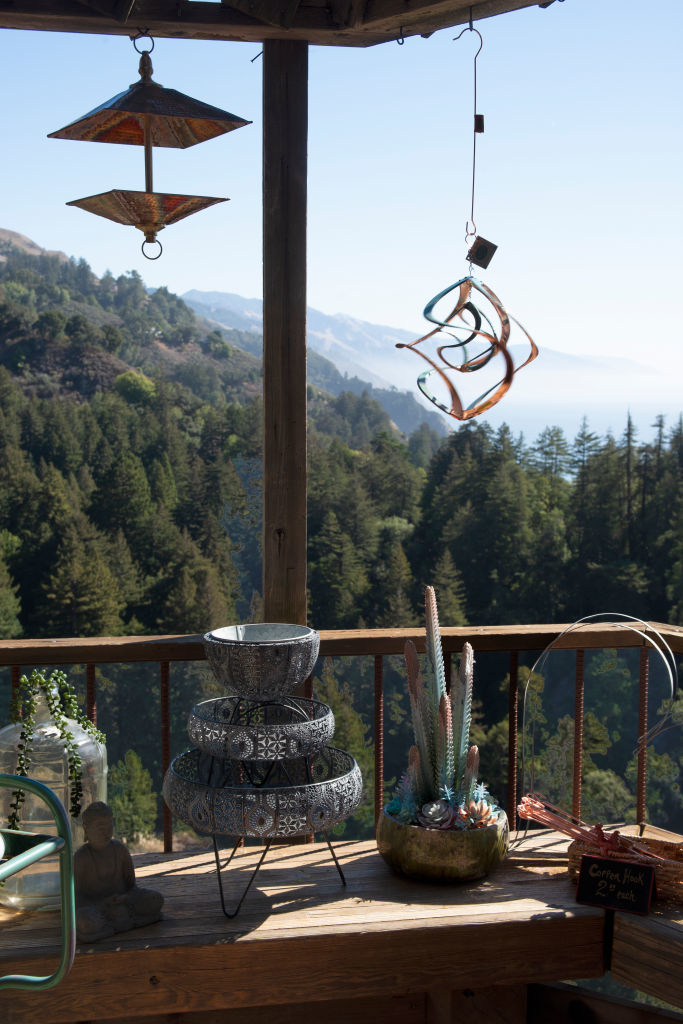 Wind chimes and potted plants on a wooden deck with a hillside and clear sky in the background