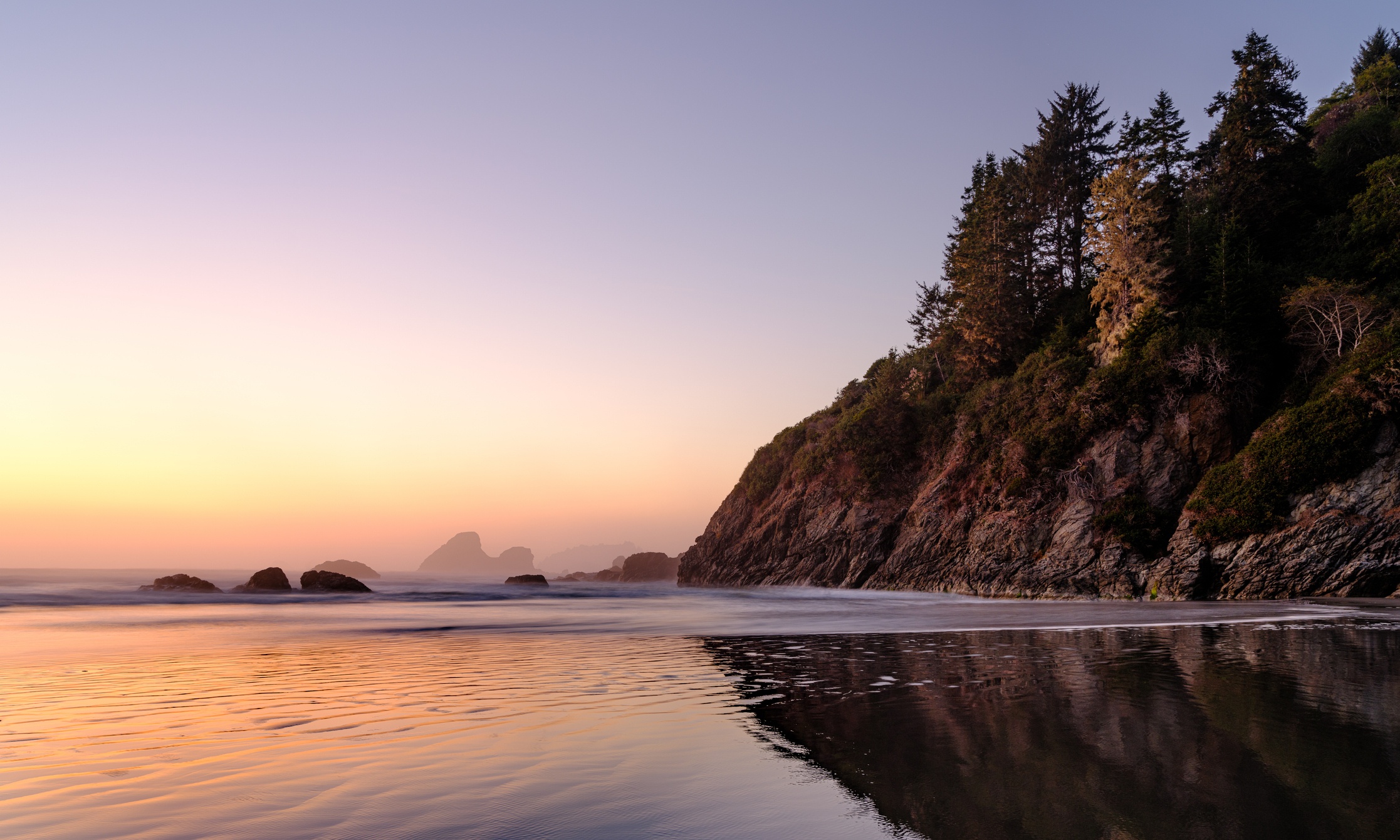 Serenity at the beach with waves gently touching the shore, surrounded by cliffs and trees at twilight