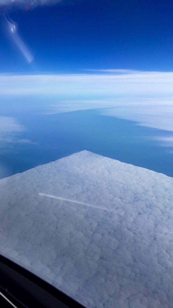 View from airplane window showing the horizon and blanket of clouds below