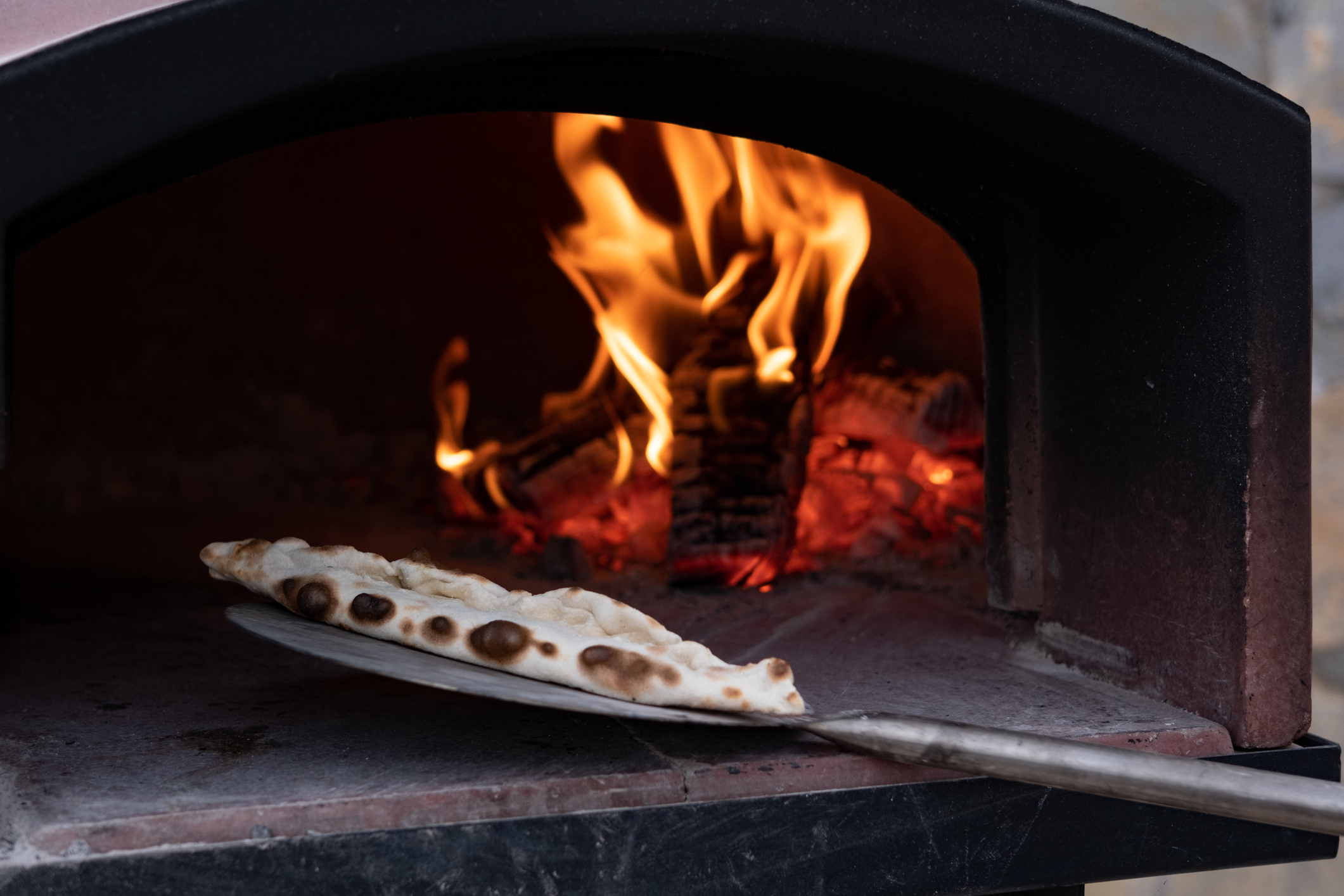 Pizza being cooked in a wood-fired oven with flames in the background