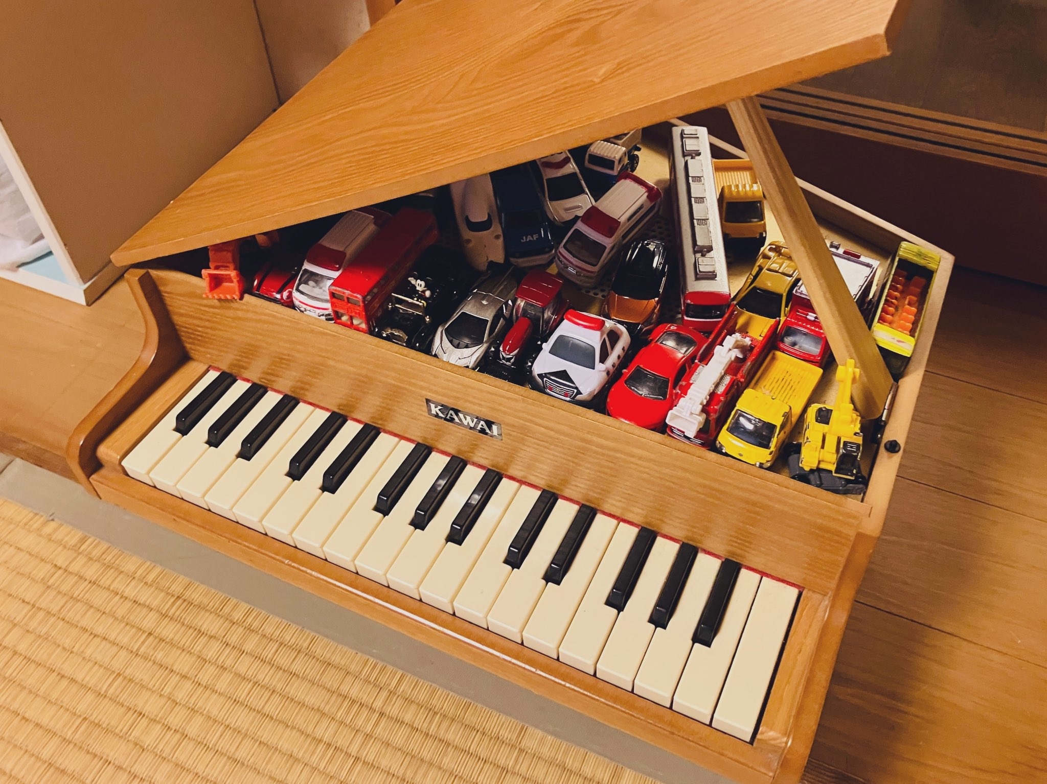 ピアノの上に様々なモデルの車のおもちゃが並べられている。
