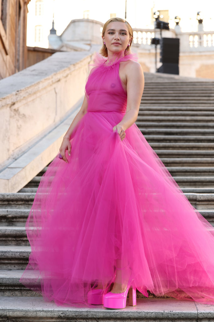 Florence Pugh poses on stairs, wearing a sleeveless, voluminous gown with a high neckline