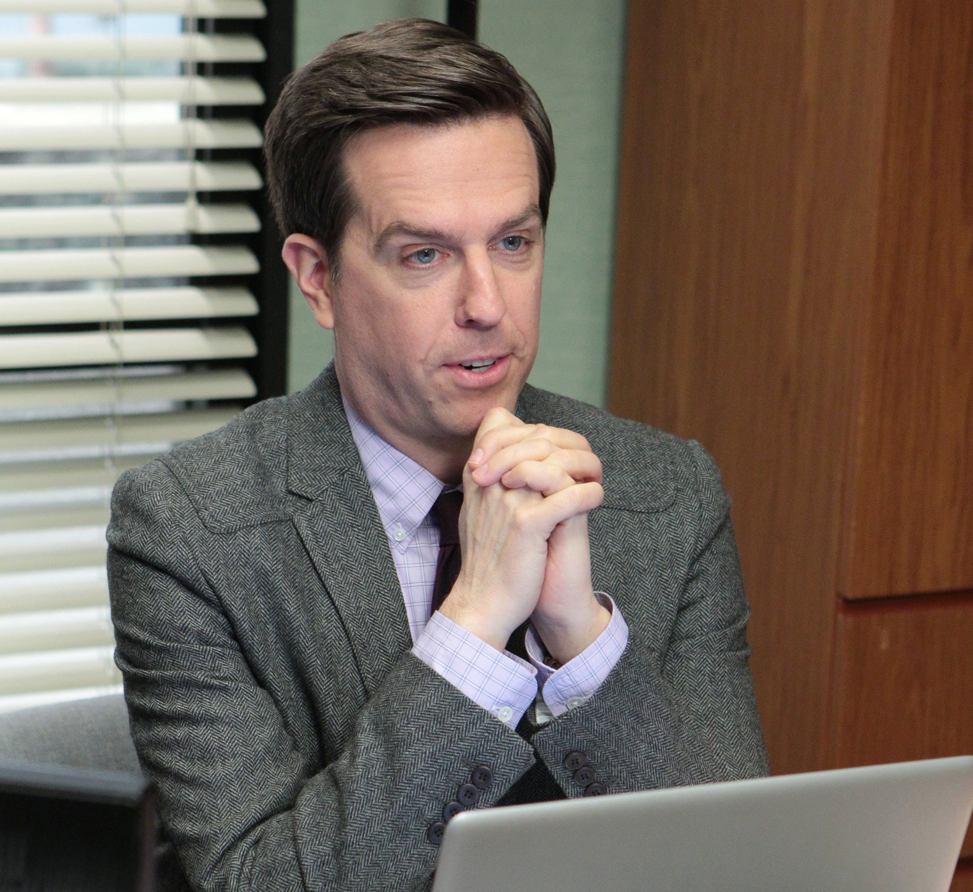 Character Andy Bernard from The Office in an office setting with a laptop and desk accessories