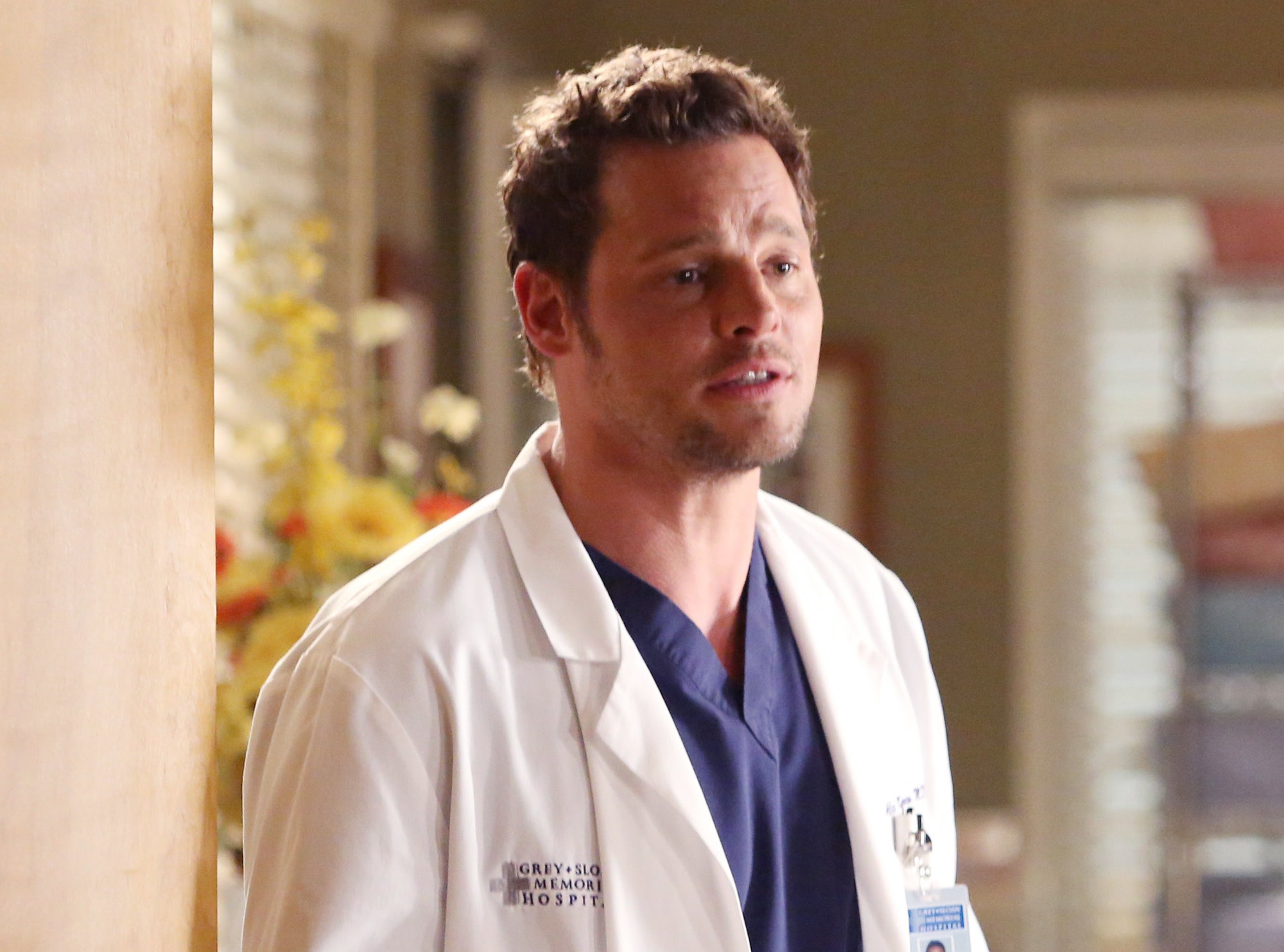 Actor in a white lab coat portraying Dr. Alex Karev on a TV show set, looking concerned