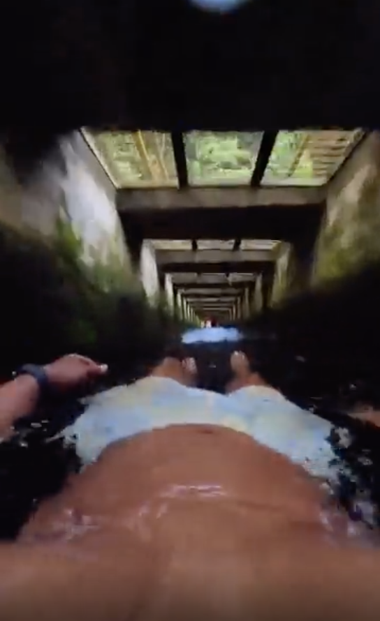 Person on a waterslide viewed from a first-person perspective, descending through a tunnel