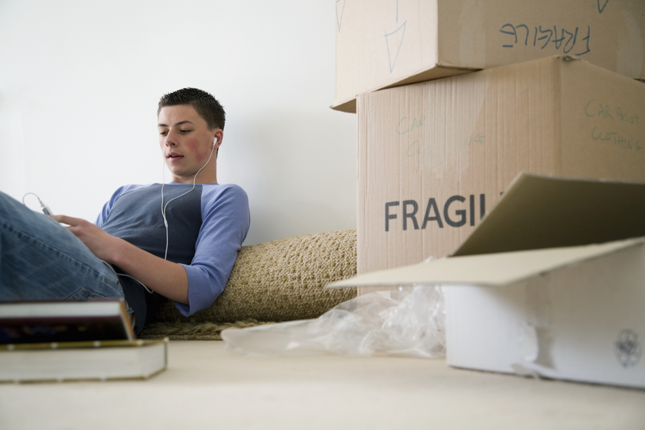 Person sitting on the floor, surrounded by moving boxes, using a device with earphones