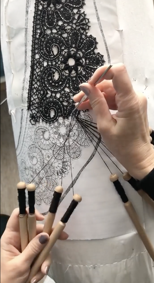 Hands crafting detailed lacework with bobbins on a patterned design