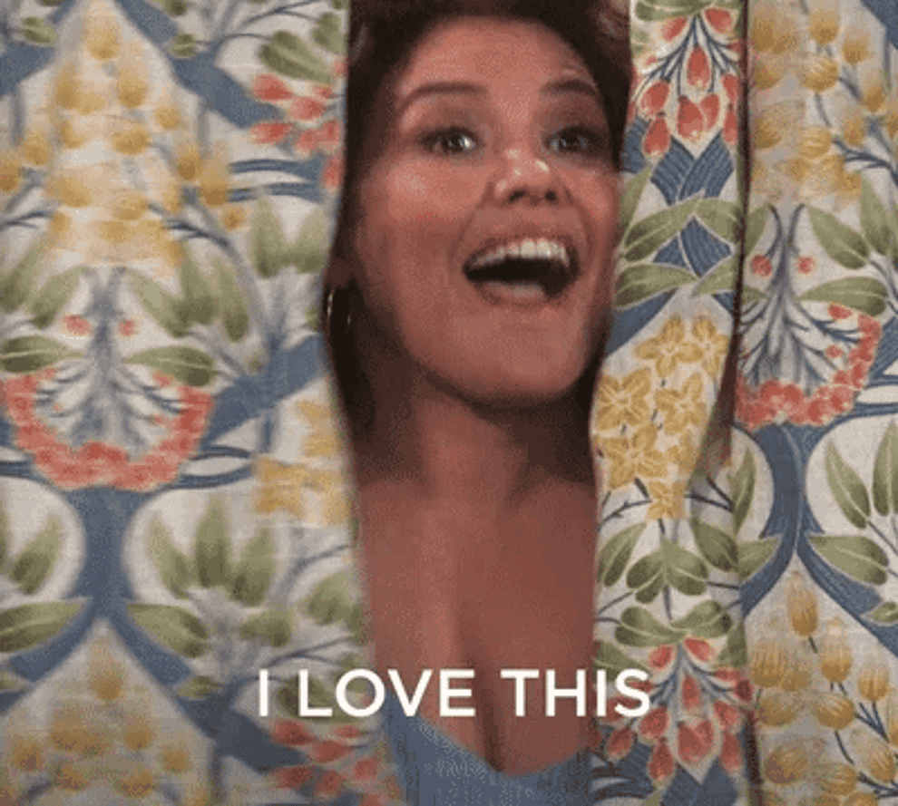 GIF of a woman popping out from behind a curtain with an excited expression, text reads &quot;I LOVE THIS&quot; above her head