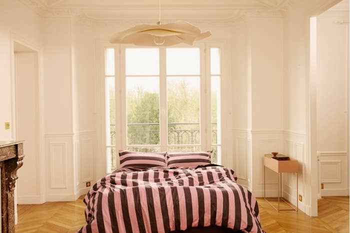 Bedroom with a bed covered in a striped blanket, large windows, and ornate decor, suggesting stylish home furnishings