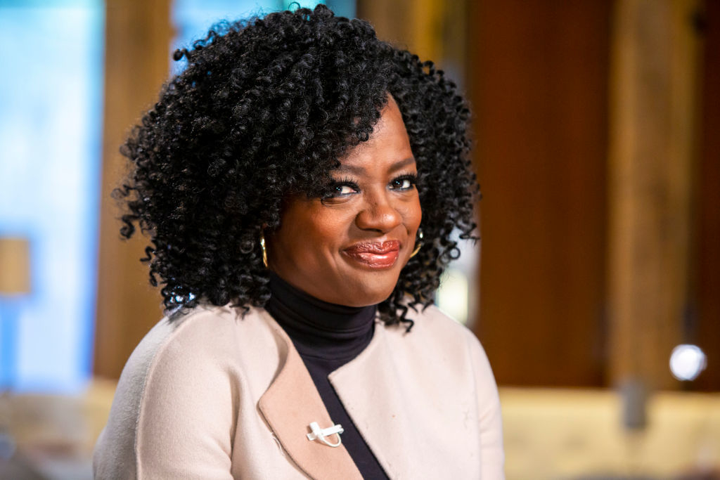 Viola Davis wearing a beige blazer and black top, with a silver brooch, smiling indoors