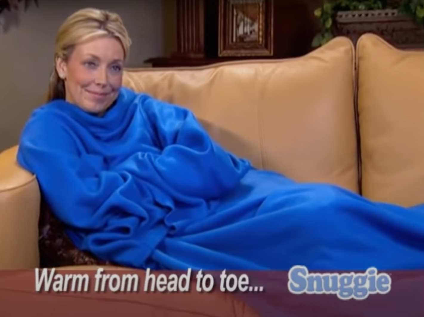 Woman in a Snuggie blanket on a couch, text advertises being &#x27;Warm from head to toe&#x27;
