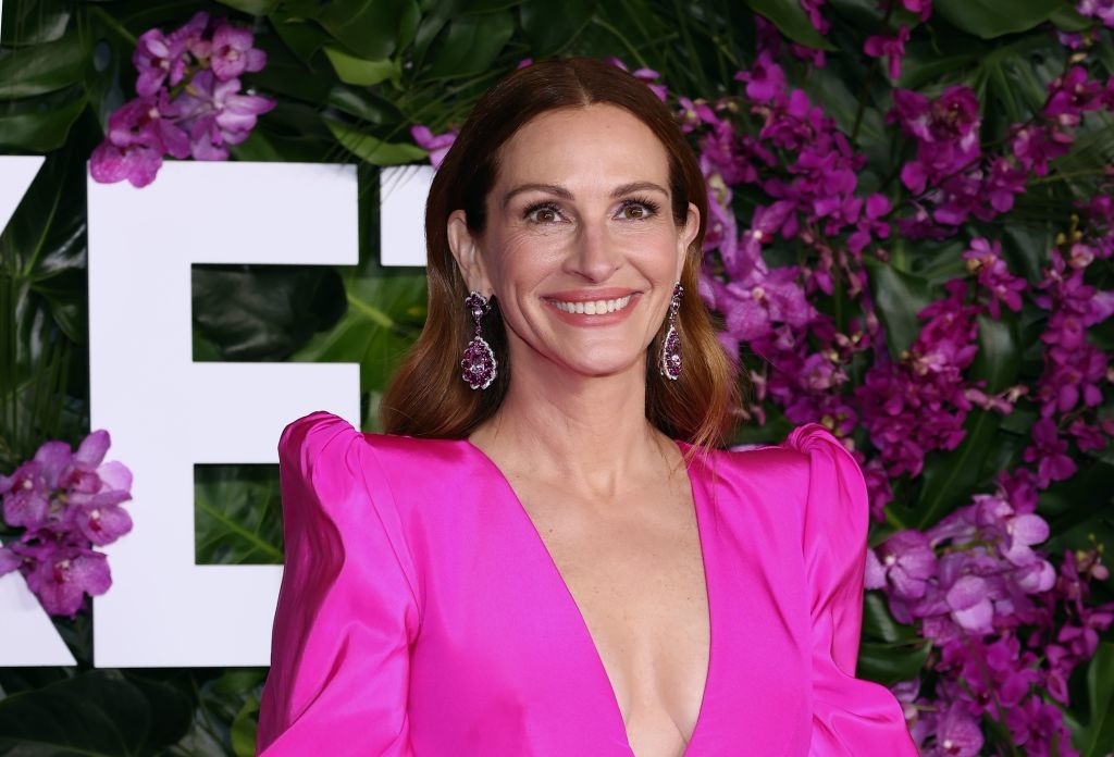 Leslie Mann in a deep v-neck gown with earrings at an event with floral background