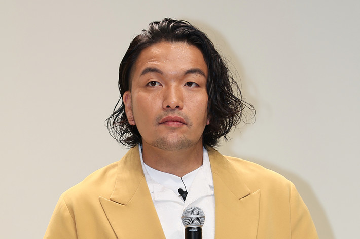 スピーチをする男性、黄色のジャケットと白いシャツ着用。