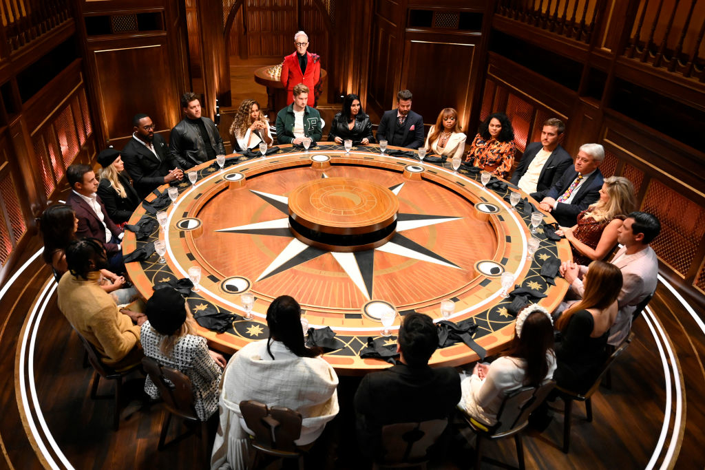 Group of people sitting around a large circular table in a conference room with a central moderator