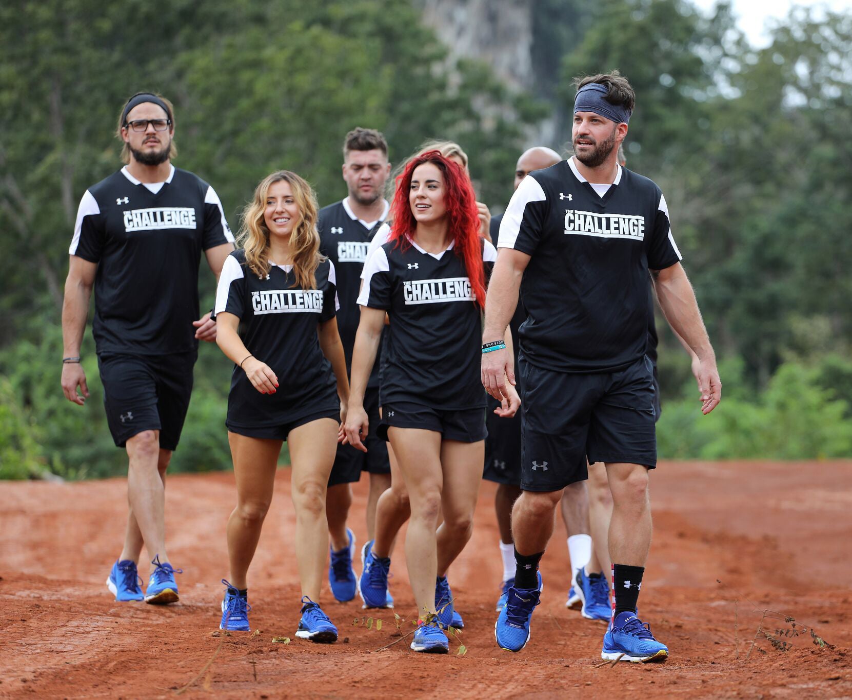 Five people in matching sports kits walk on a dirt path
