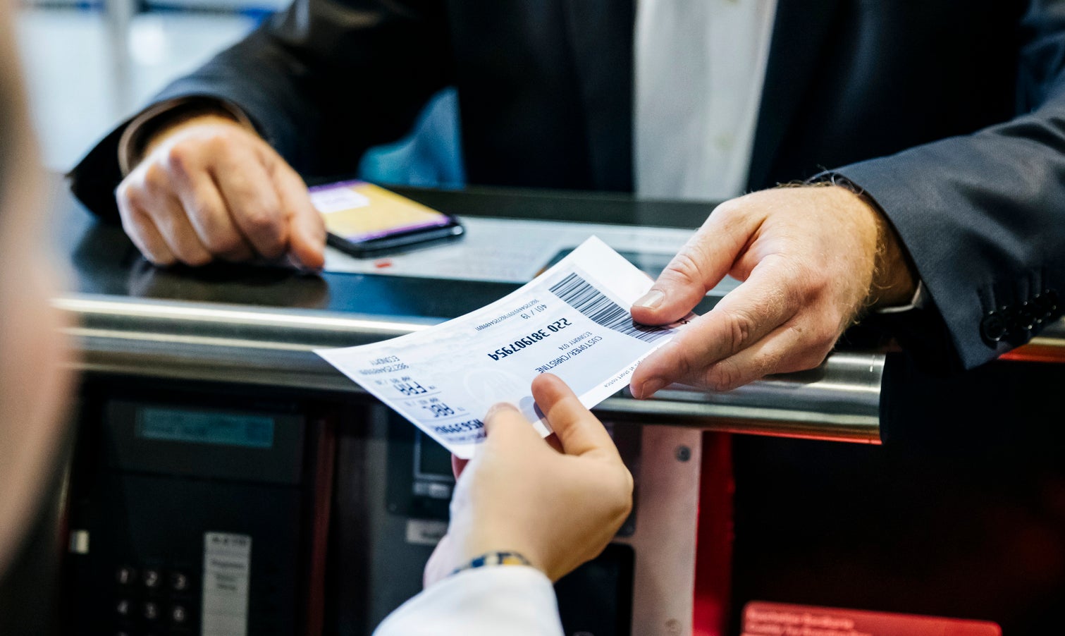 Person at airport check-in counter handing over a boarding pass to an airline representative