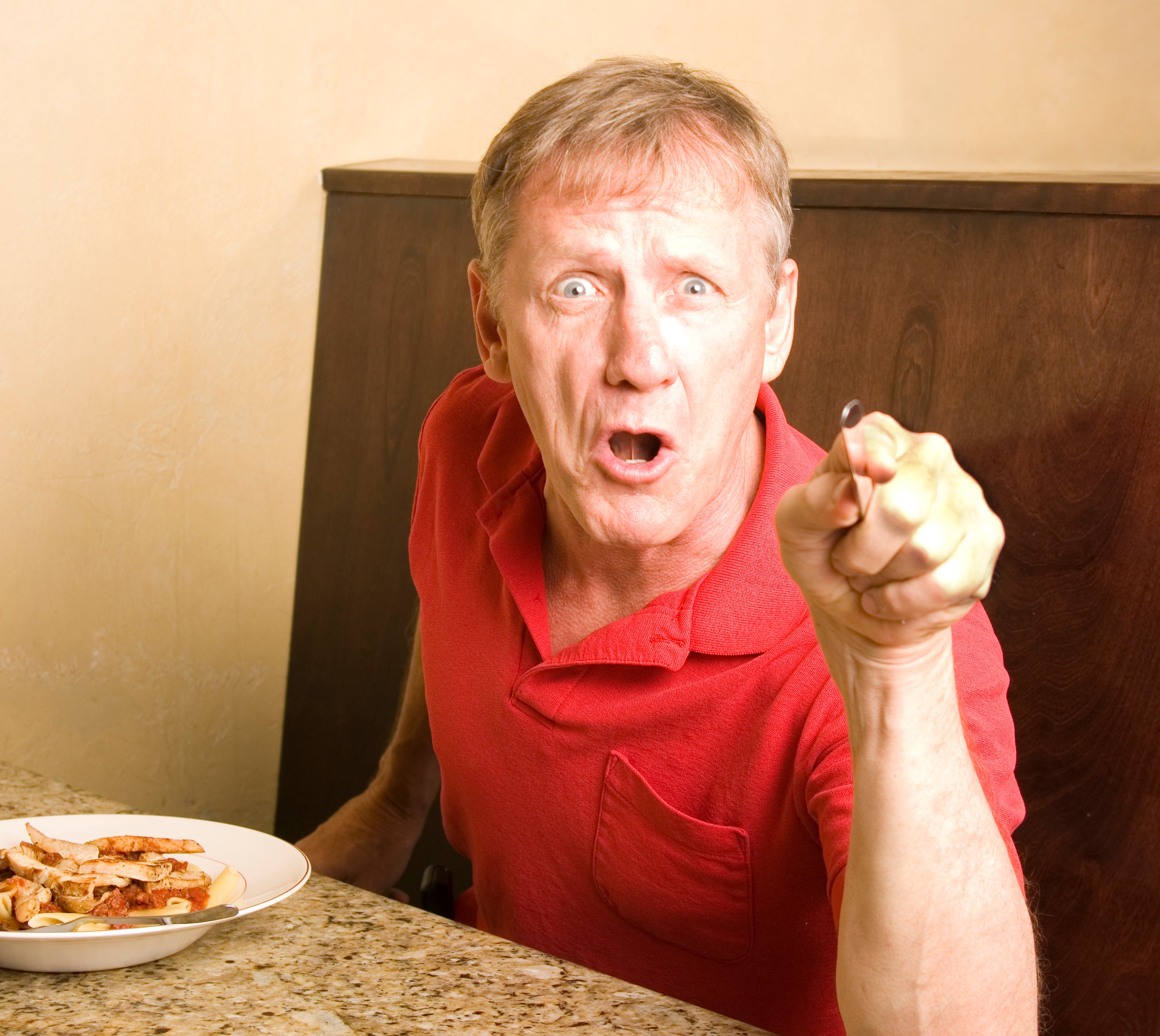 Man gesturing with a fork at a dining table, expressing surprise or excitement