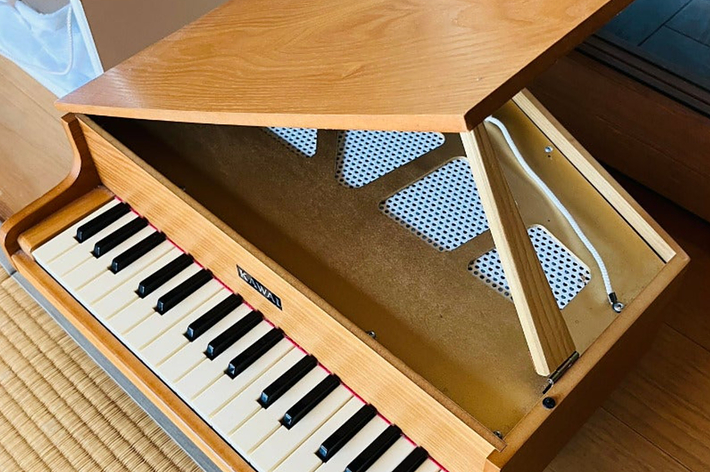 木製のアップライトピアノの上部が開いていて、内部の鍵盤とペダルが見えます。