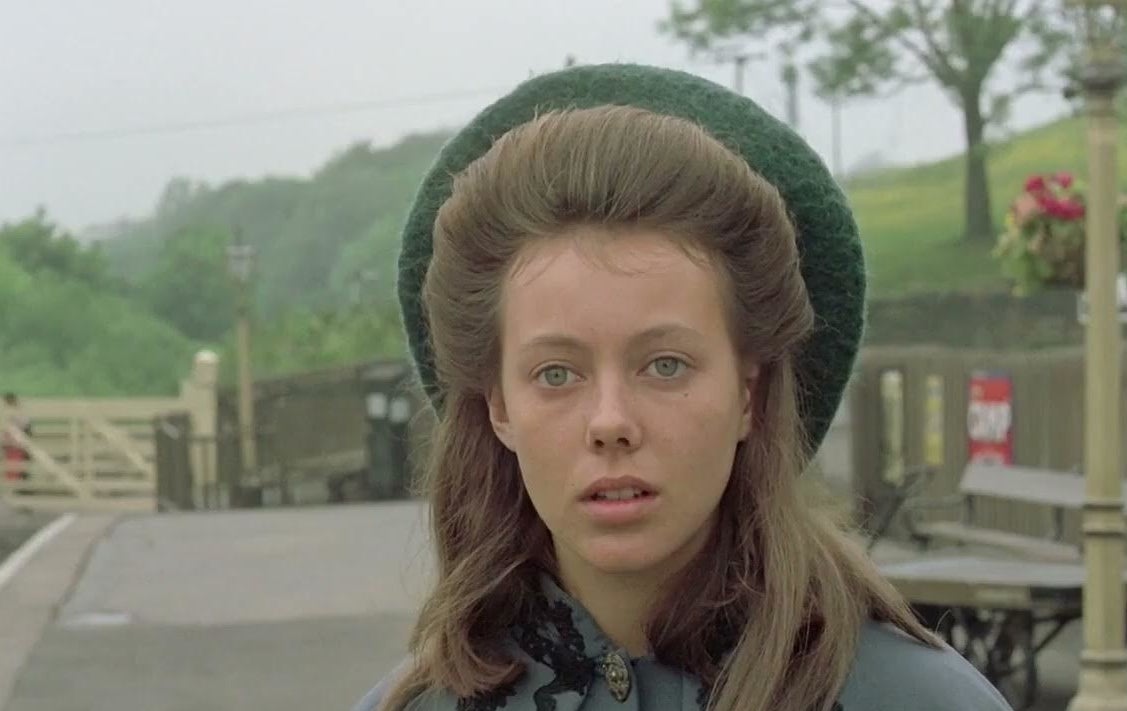 Close-up of a female character from an older film, outdoors, wearing a green beret