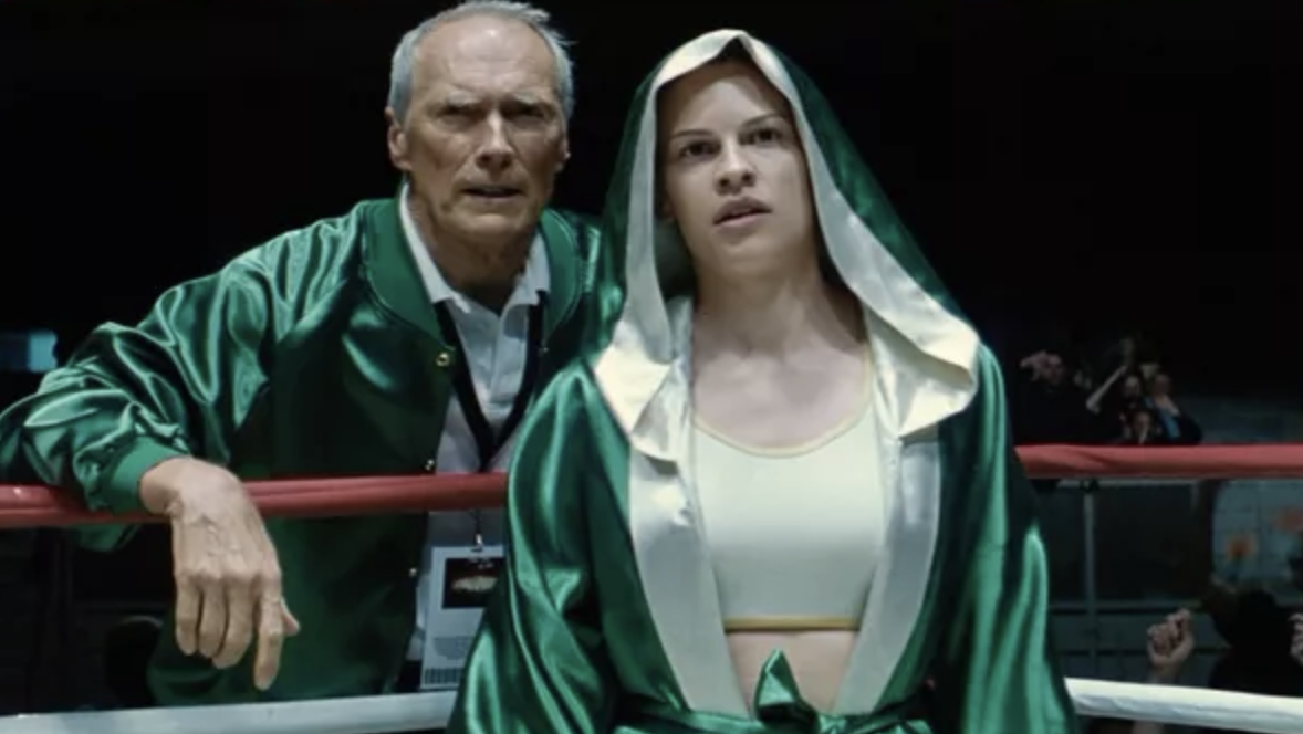 Frankie Dunn and Maggie Fitzgerald characters in a boxing ring corner, wearing sports attire, with a concerned expression