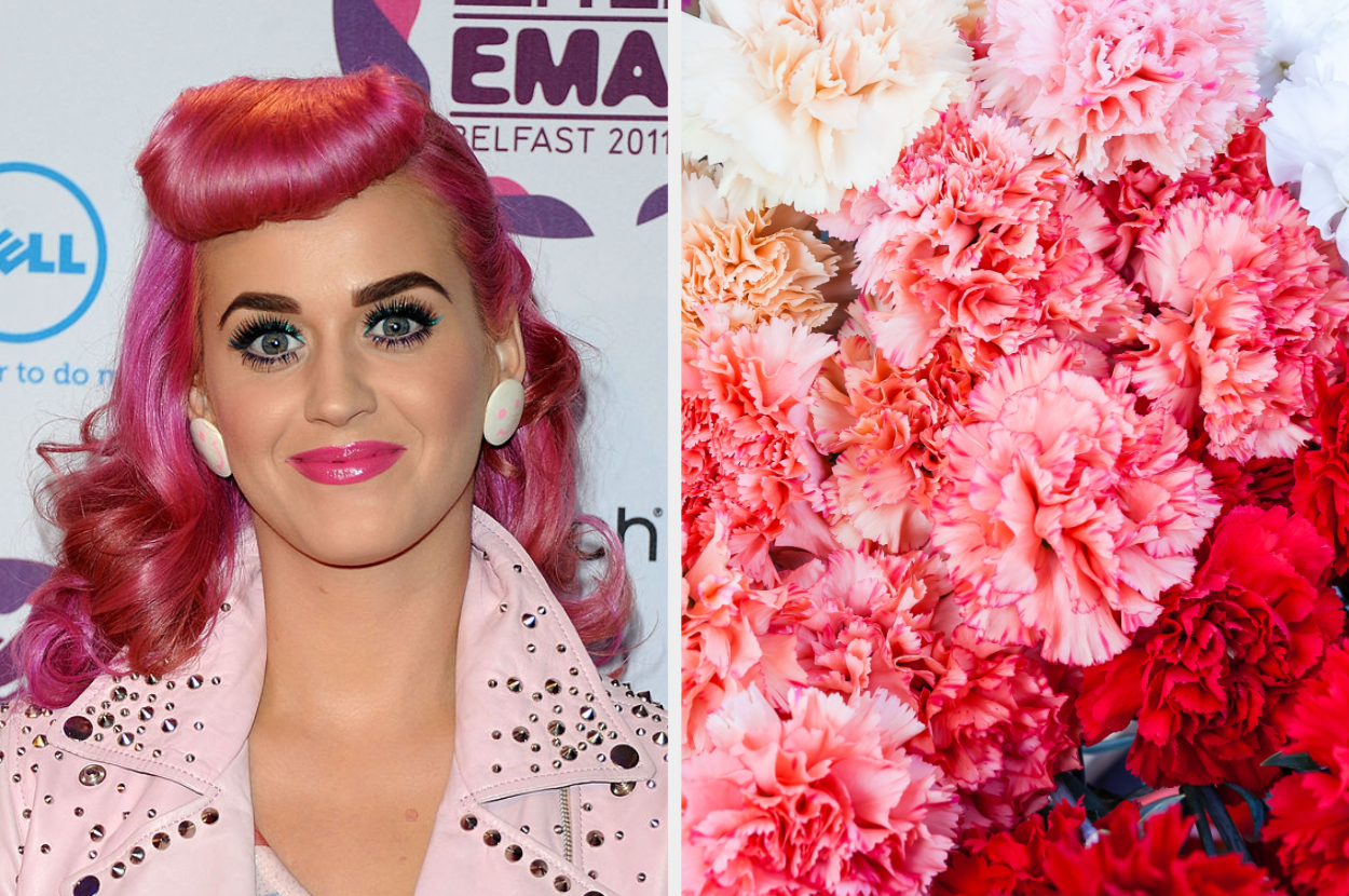 Person with pink hair styled in a wave, wearing pink jacket and earrings, beside a wall of pink and red blooms