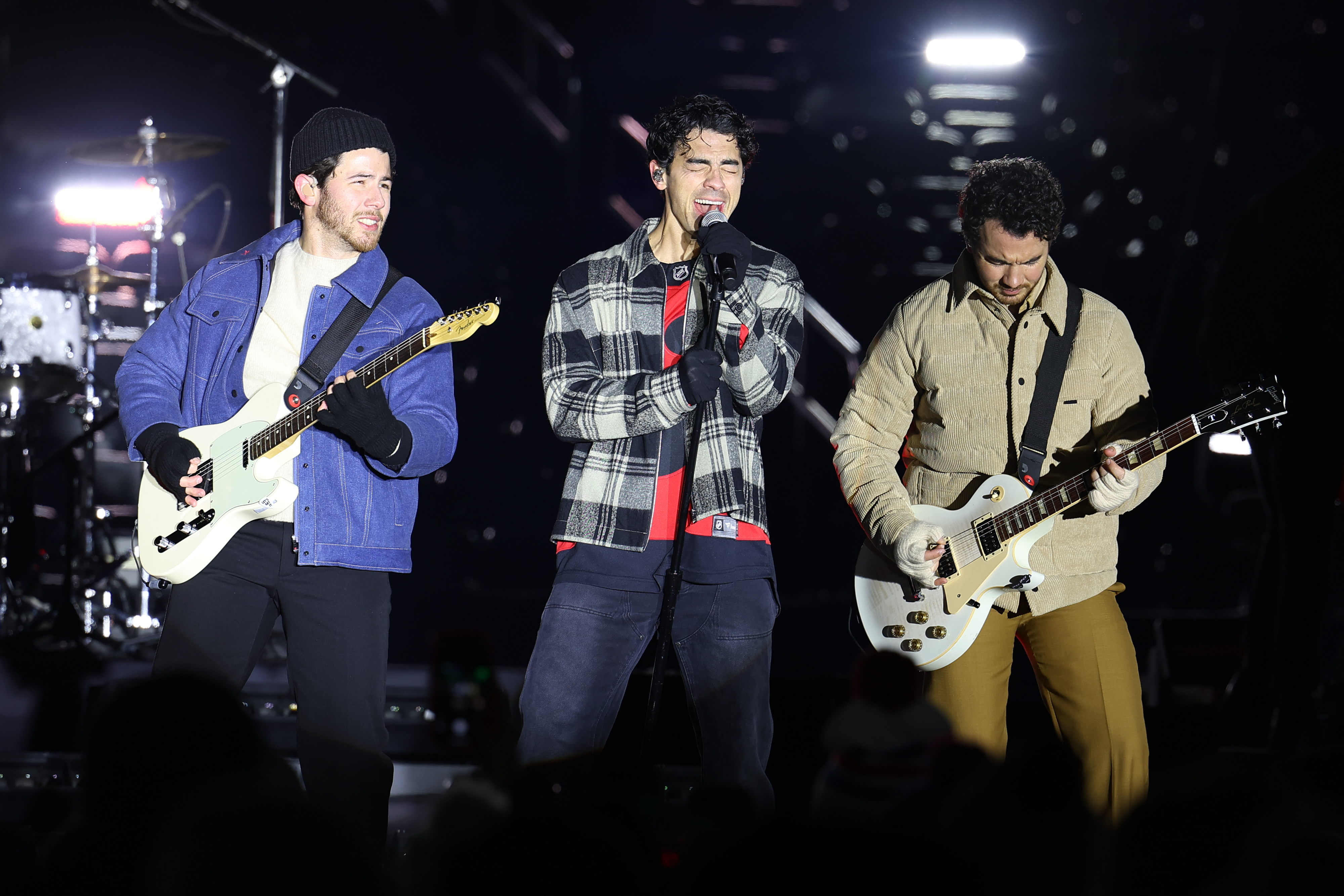 The Jonas Brothers perform on stage with guitars and a microphone