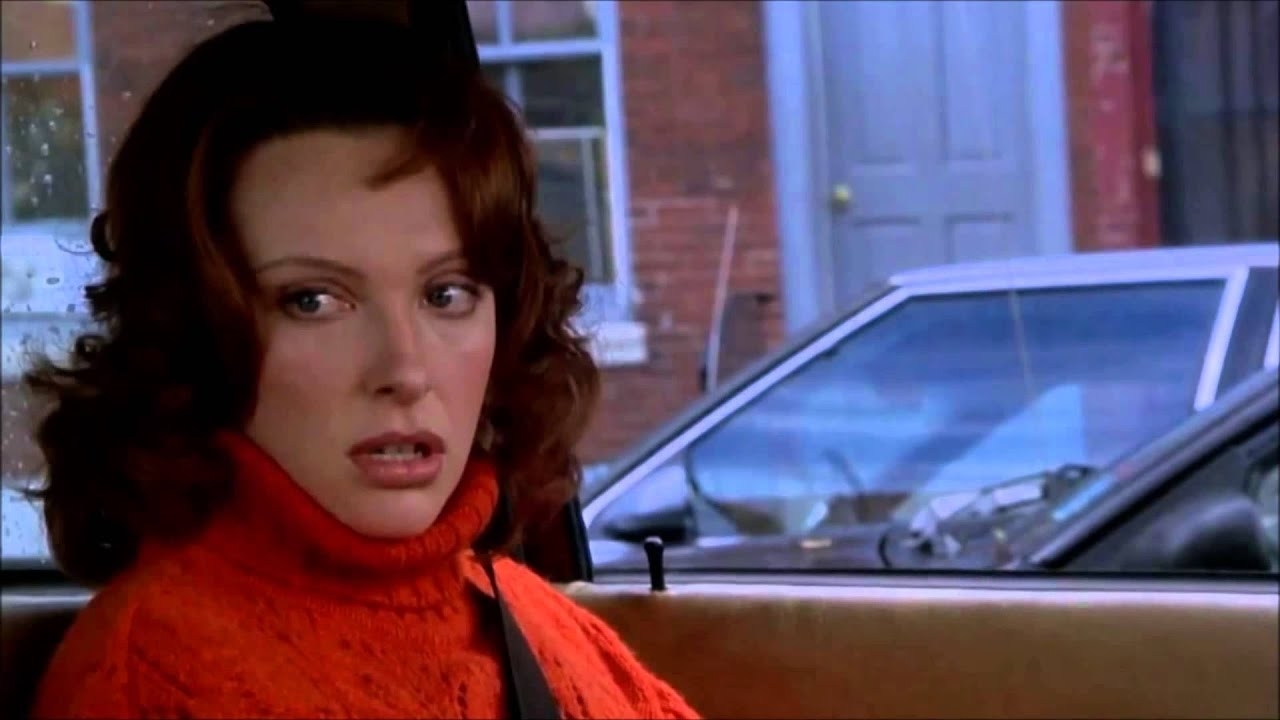 Grace Adler from the TV show &quot;Will &amp;amp; Grace&quot; wearing a chunky, textured orange turtleneck, seated in a car, looking surprised