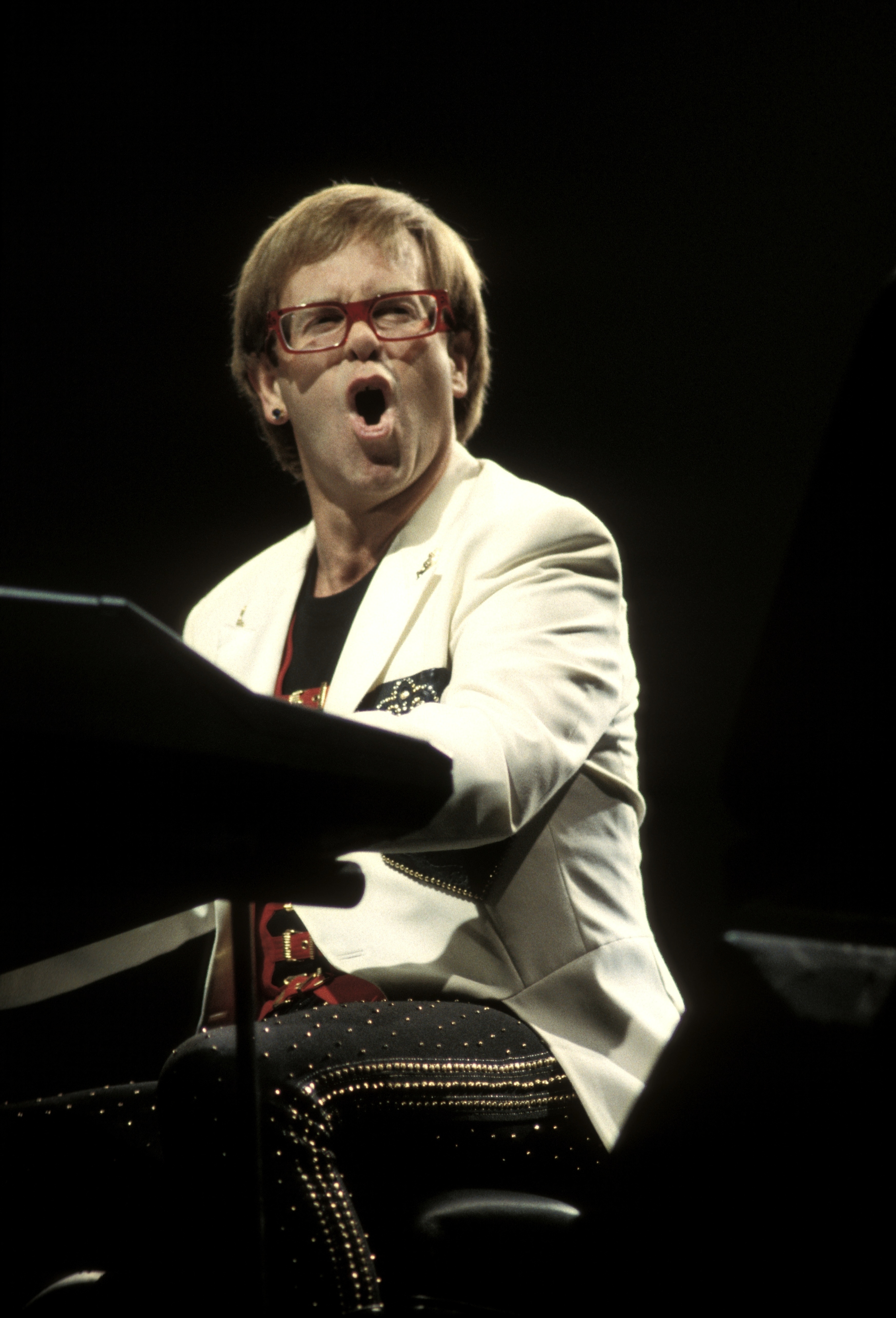 Elton John in performance attire at the piano, singing with emotion
