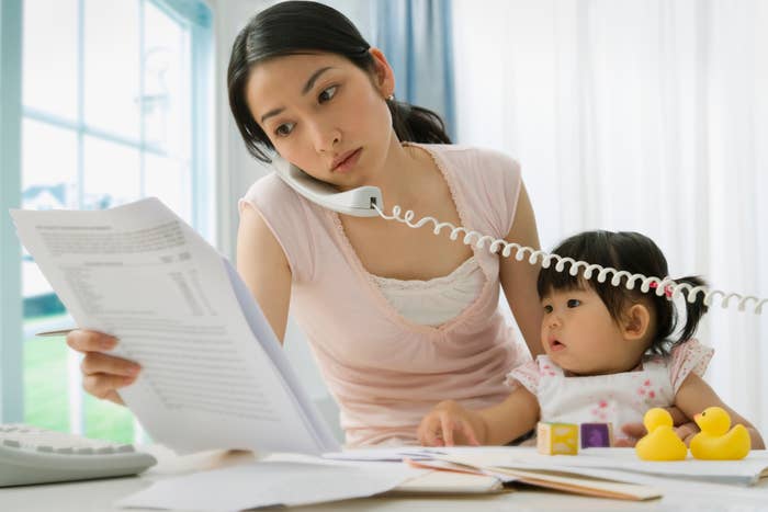 女性が電話をしながら書類を読み、幼児が見つめています。