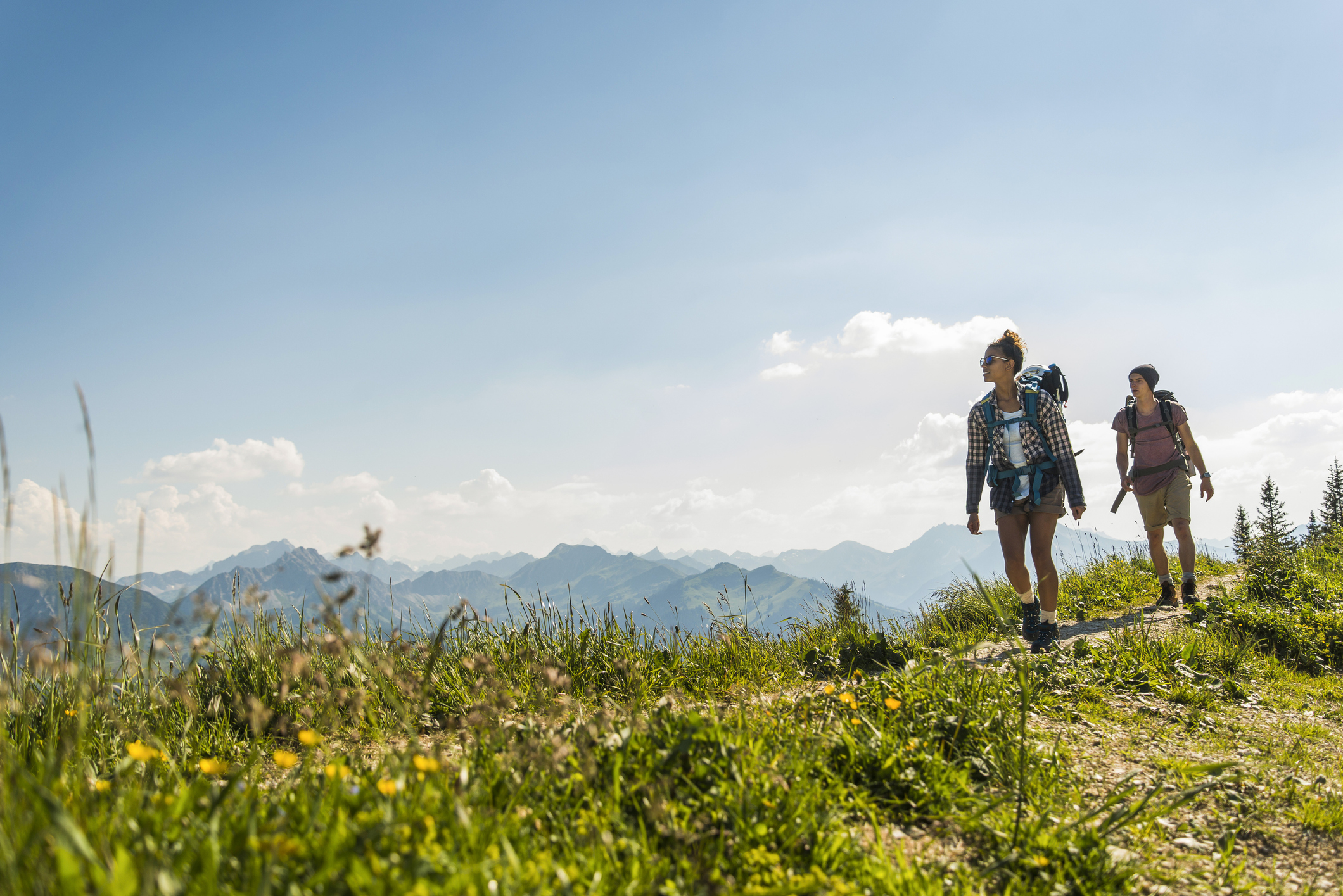 Two hikers with backpacks walking on a mountain trail with distant peaks