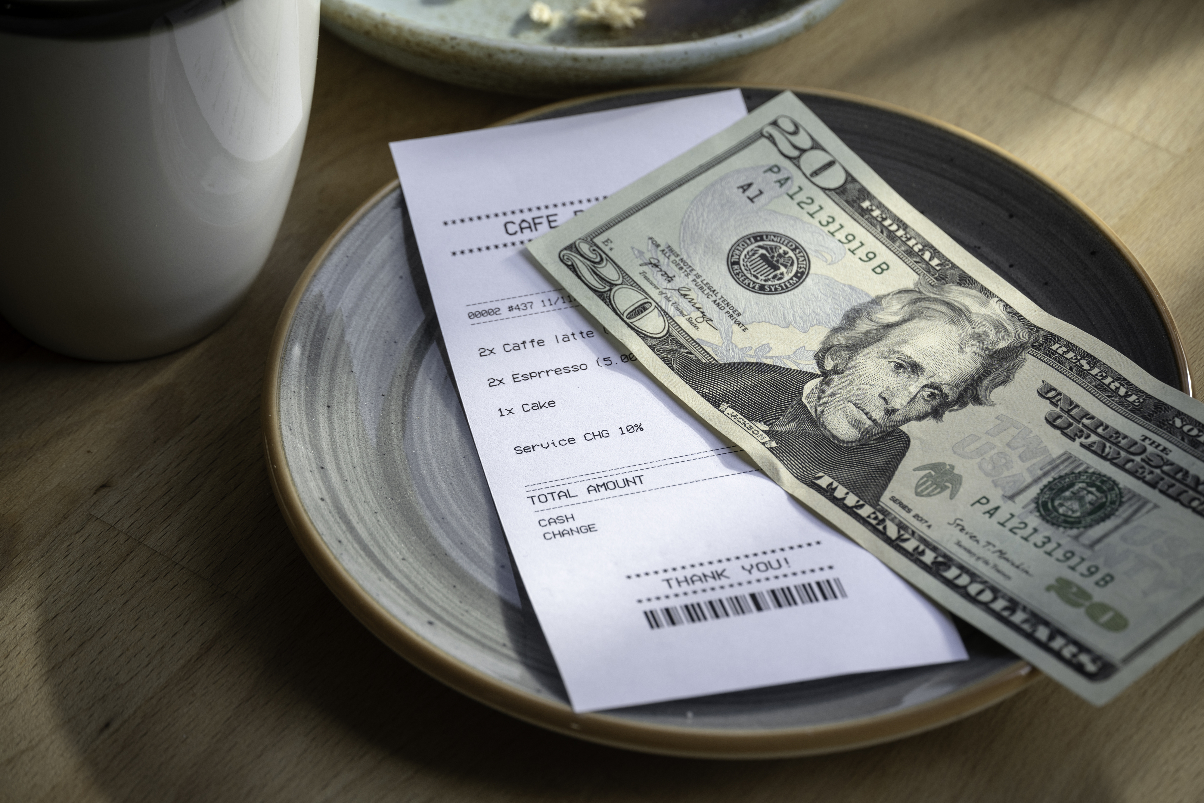 A receipt on a plate with a $20 bill, indicating a payment for a café latte and espresso