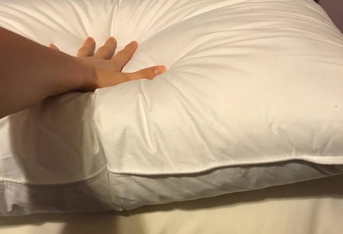 Person&#x27;s hand pressing a memory foam pillow, demonstrating its softness and texture