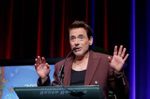 Robert Downey Jr at podium speaking at an event with his hands raised expressively