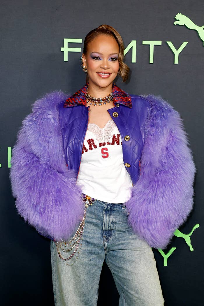 Rihanna stands confidently wearing a feathered coat and jeans at a Fenty event