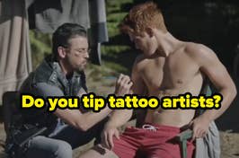 Man applying makeup to another shirtless man on a film set, with motorcycle in background