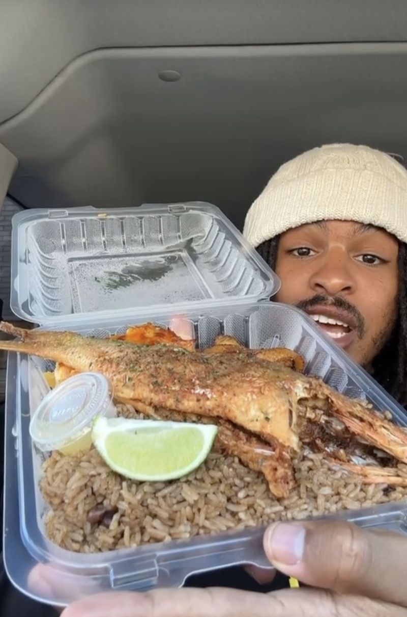 Keith showing a takeout container with rice and grilled fish, wearing a beanie