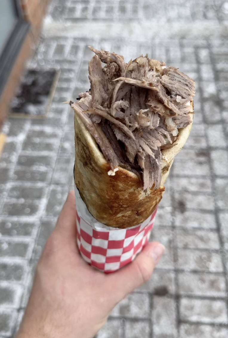 A person holding a cone filled with pulled meat, wrapped in a flatbread, over a cobblestone street