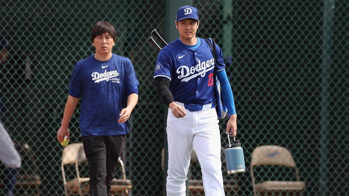 Two baseball players in Dodgers uniforms walking on the field, one carrying a bat