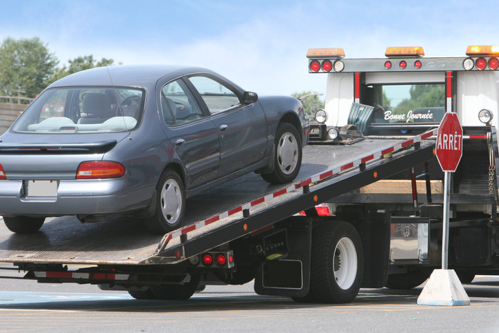 A car being towed onto a flatbed tow truck with an &quot;Arret&quot; sign, French for &quot;Stop,&quot; visible
