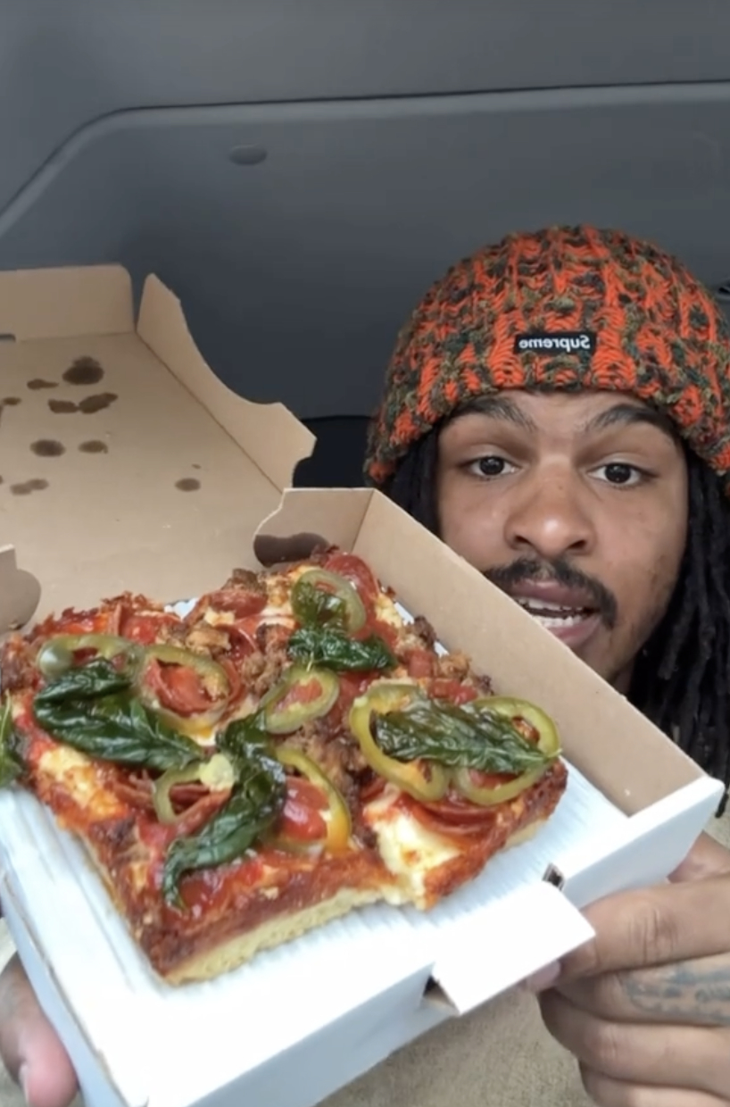 Keith Lee holding a pizza box with one slice left, wearing an orange-patterned beanie