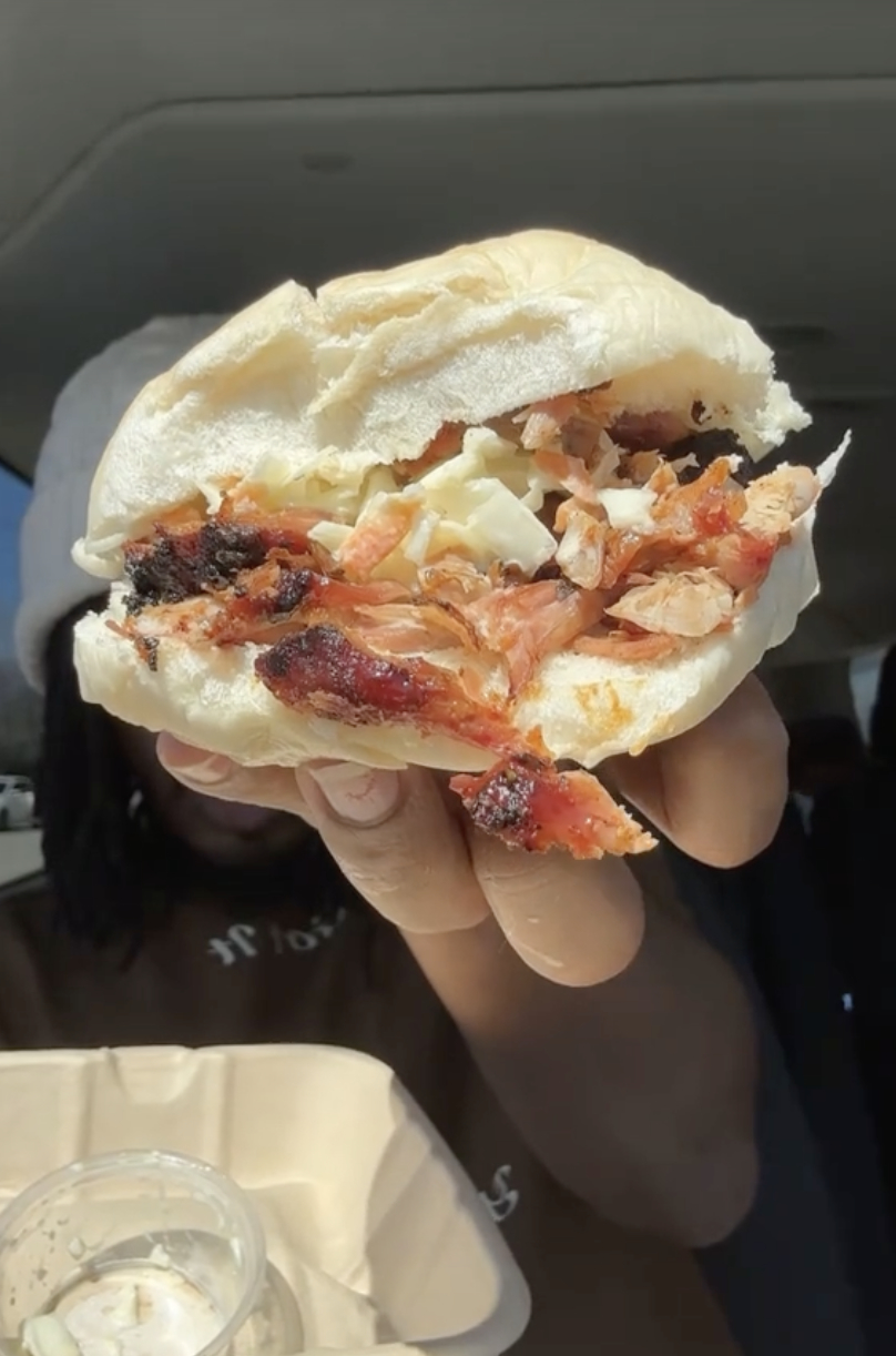 Close-up of a hand holding a sandwich with chicken and coleslaw