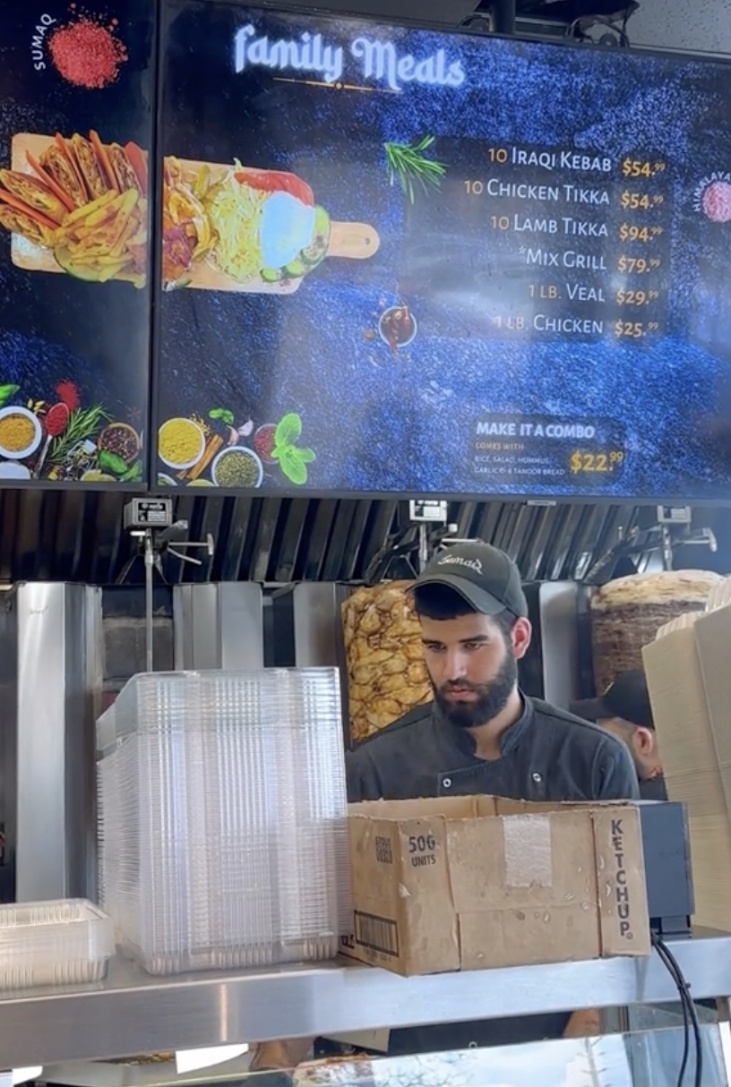 Menu board with various meal options and prices above a person working at a food counter